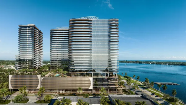 Buildings stand on a bright, sunny day on the waterfront. There is an abundance of green space around the building, and the buildings are modern, and covered with windows.