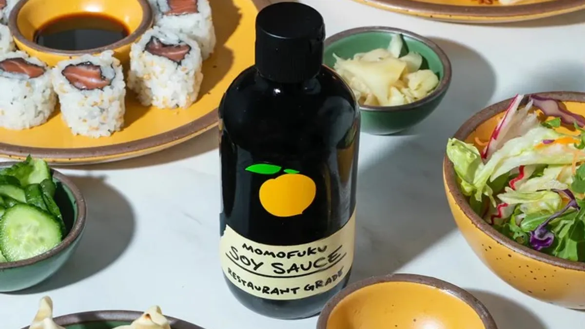 A clear soy sauce bottle with brown sauce on a table surrounded by food and plates