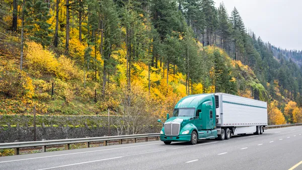 A reefer driving on highway road with autumn foliage on hills in the background.