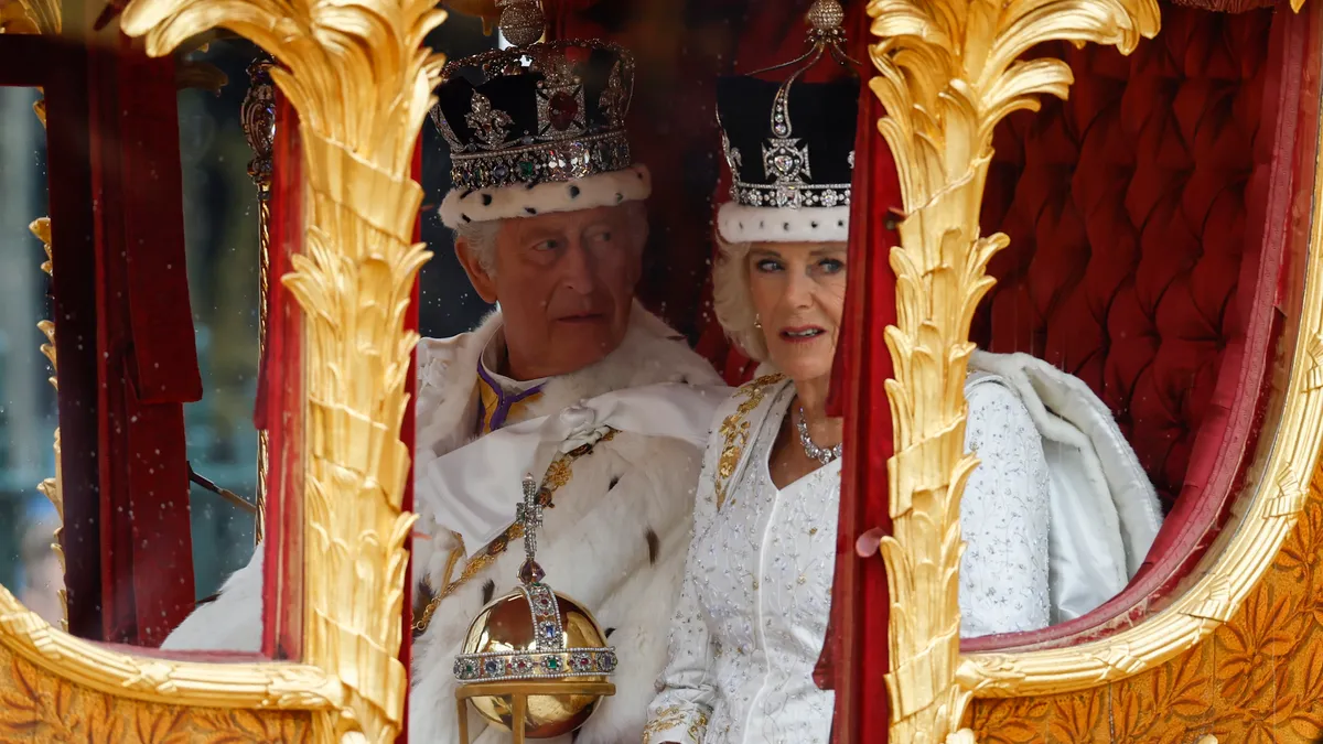 King Charles and queen Consort Camilla in white coronation attire arrive in a gold carriage.