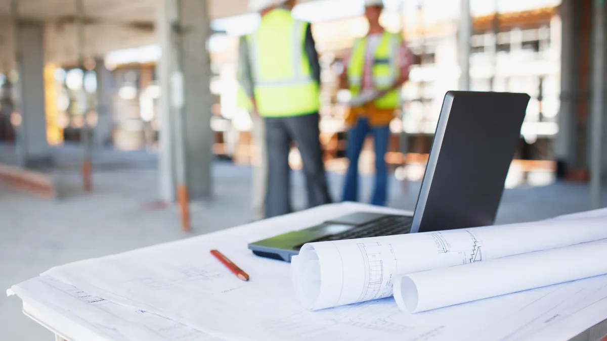 Construction workers in the background, while a laptop and office supplies are in the foreground.