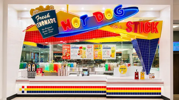 A photograph of a white storefront with neon signs that say Hot Dog on a Stick