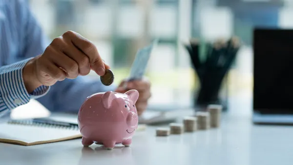 Business man putting coins in a piggy bank next to a laptop.