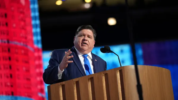Illinois Gov. J.B. Pritzker speaks into a microphone behind a wooden podium on stage at the Democratic National Convention at the United Center on August 20, 2024 in Chicago, Illinois