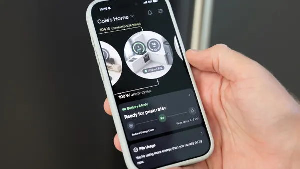 A hand holding a phone with an app showing "Cole's home" and various energy resources