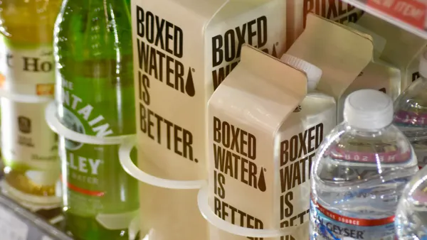 Cartons of water with Boxed Water is Better branding are next to glass and plastic water bottles in a store cooler.