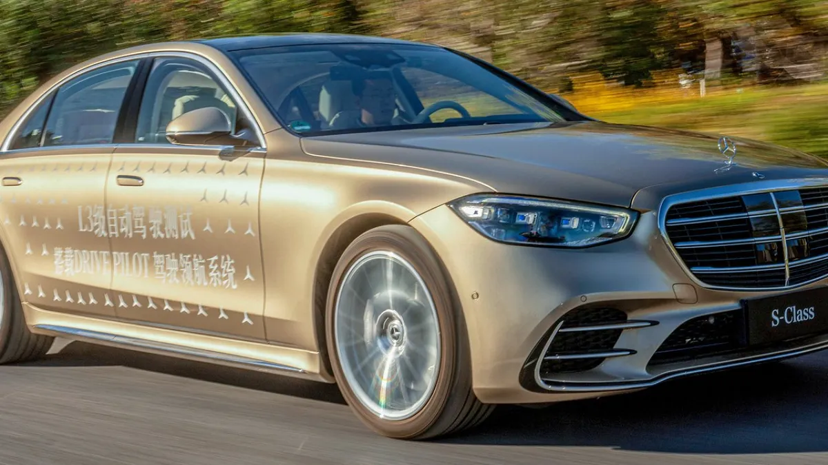 A Mercedes-Benz S-Class sedan on the highway with a Drive Pilot sticker on the driver front door.