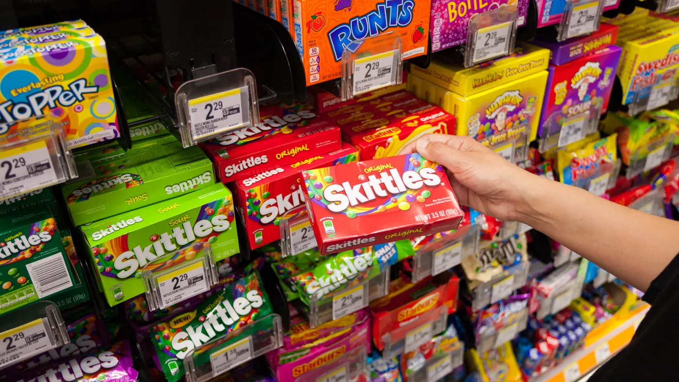 A hand is seen grabbing a package of Skittles candy