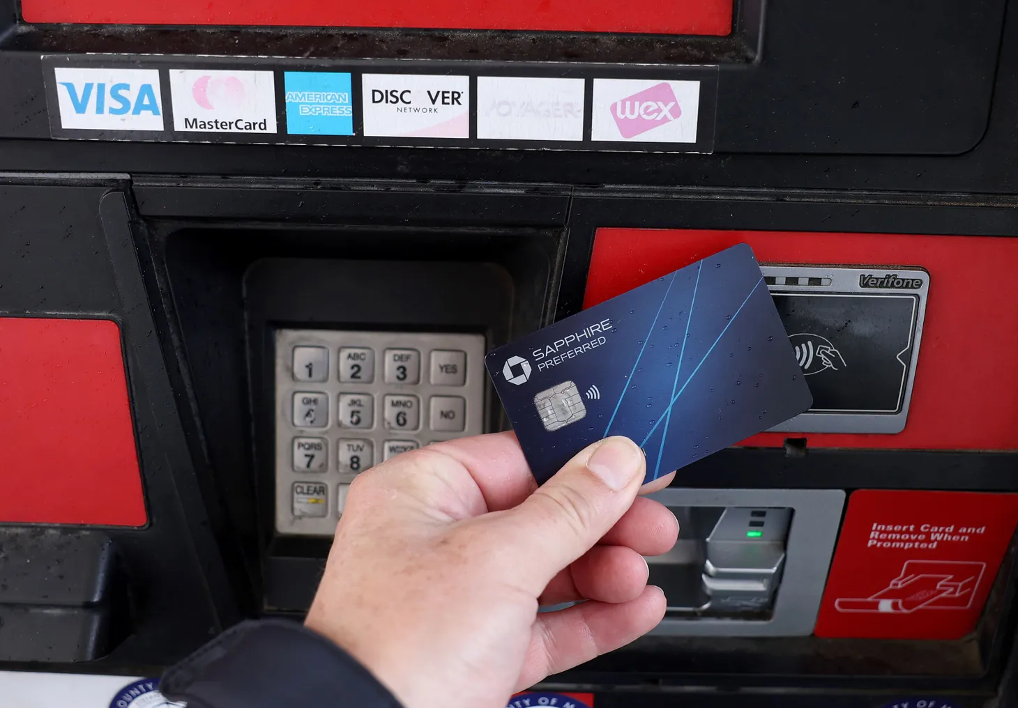 Hand holding Saphire Preferred credit card reaches to tap the card at a fuel pump.