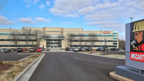 A building sits in the background under a blue sky. A red sign, made of stone, is to the right, which says "McCarthy."