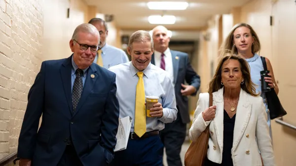 A handful of people are walking toward the camera. They are walking in a hallway