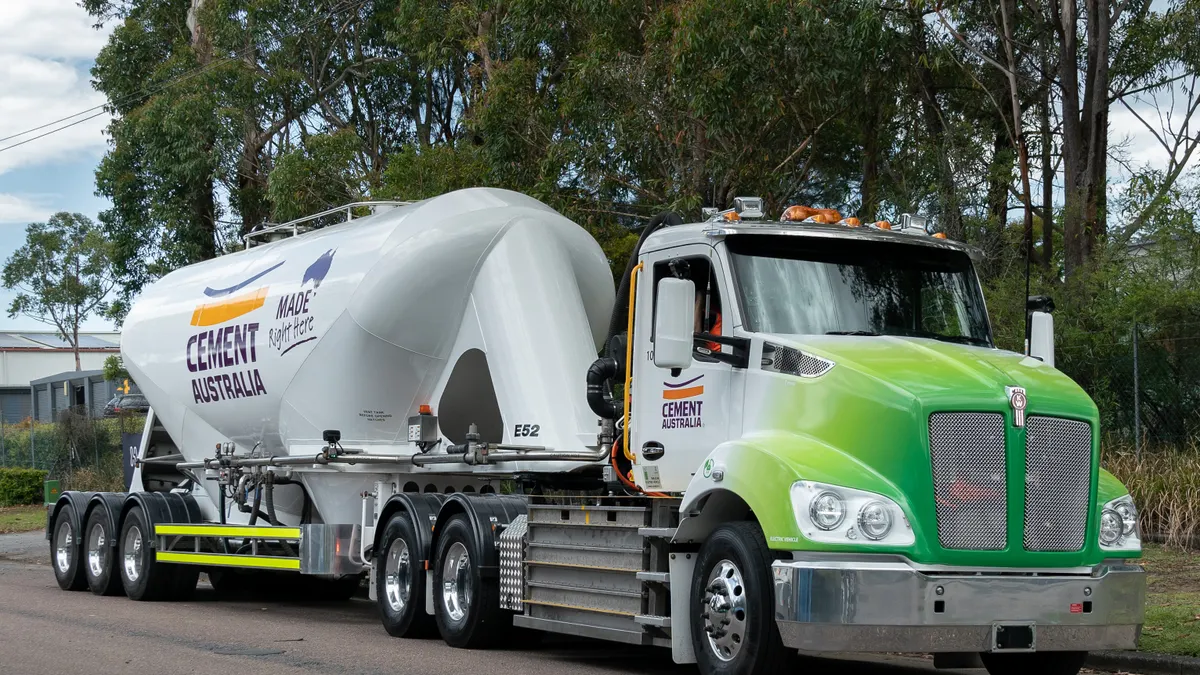 A Cement Australia battery-electric truck on a road near a line of trees.