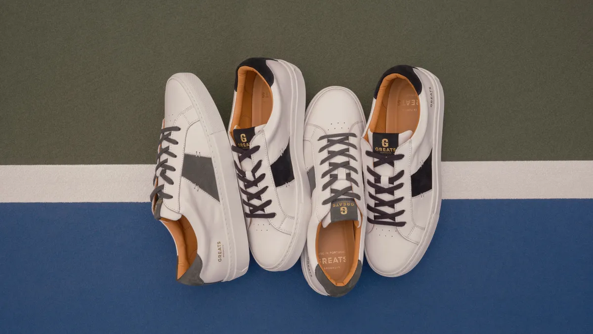 Four white sneakers with contrasting dark stripes are posed on a tri-tone background.