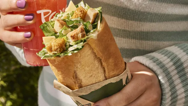 A hand holds a bread roll from Panera with a salad inside