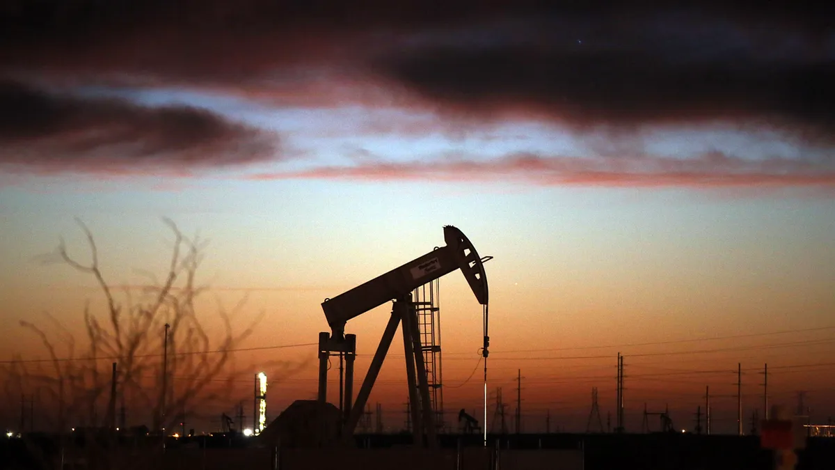 An oil pumpjack works at dawn in an oil field.