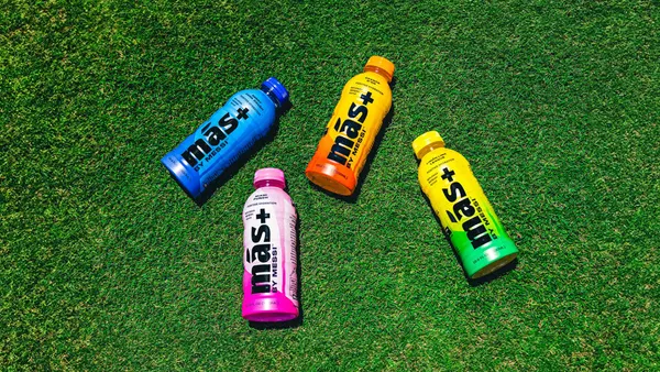 Four bottles of Mas+ by Messi on soccer turf.