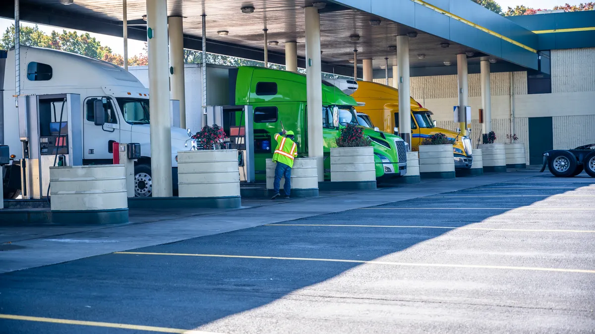 A trucker is seen near a row of semis at a truck stop awning.