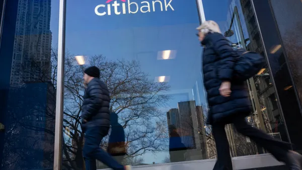 Two people walk by a Citi branch in a downtown setting