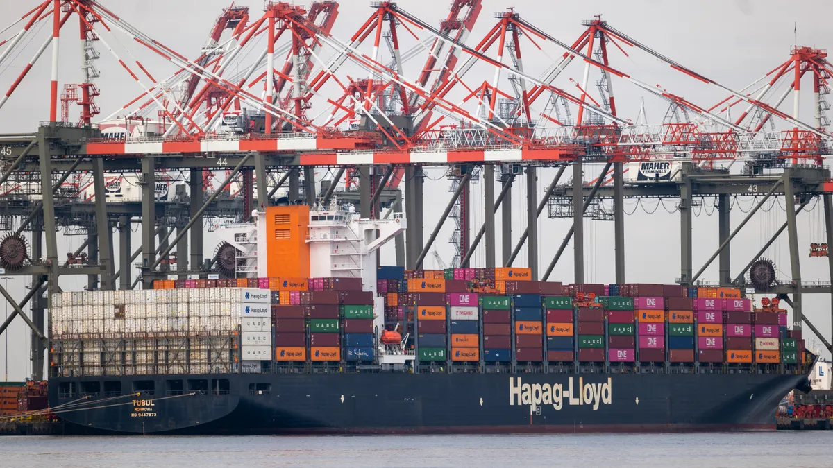 Cranes stand over shipping containers at a water port.