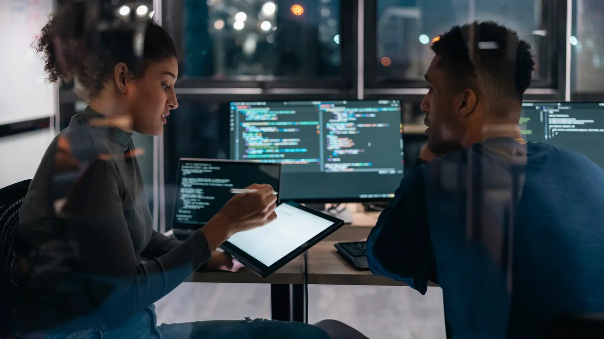Two Software developers in modern office collaborating analysing the coding on computer screen.