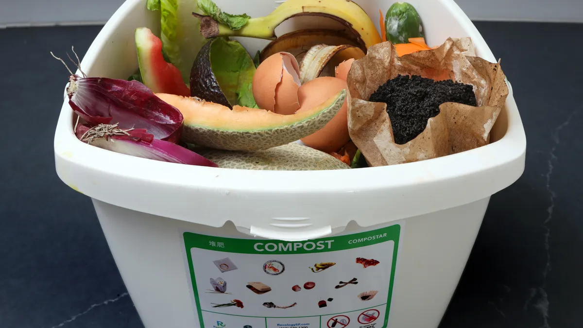 A small white plastic pail with food scraps and a label on composting guidelines