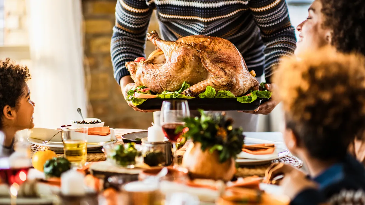 Unrecognizable black father carrying Thanksgiving turkey while serving it for his family in dining room.