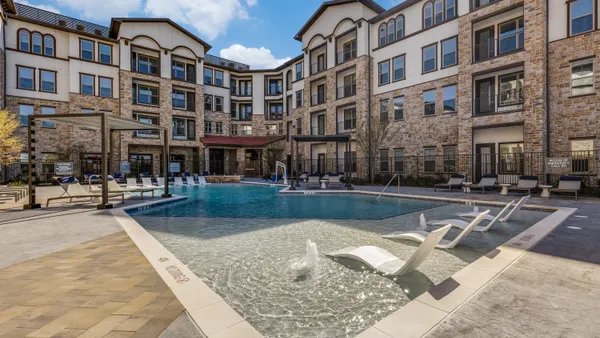 Four-story brown apartment building with a pool on the foreground.