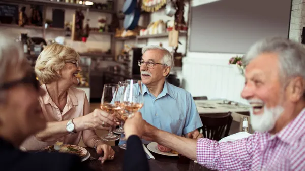 An image of people with gray hair holding up wine glasses while at a restaurant