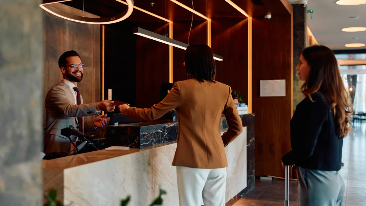 A hotel concierge hands a key to a customer at the front desk.
