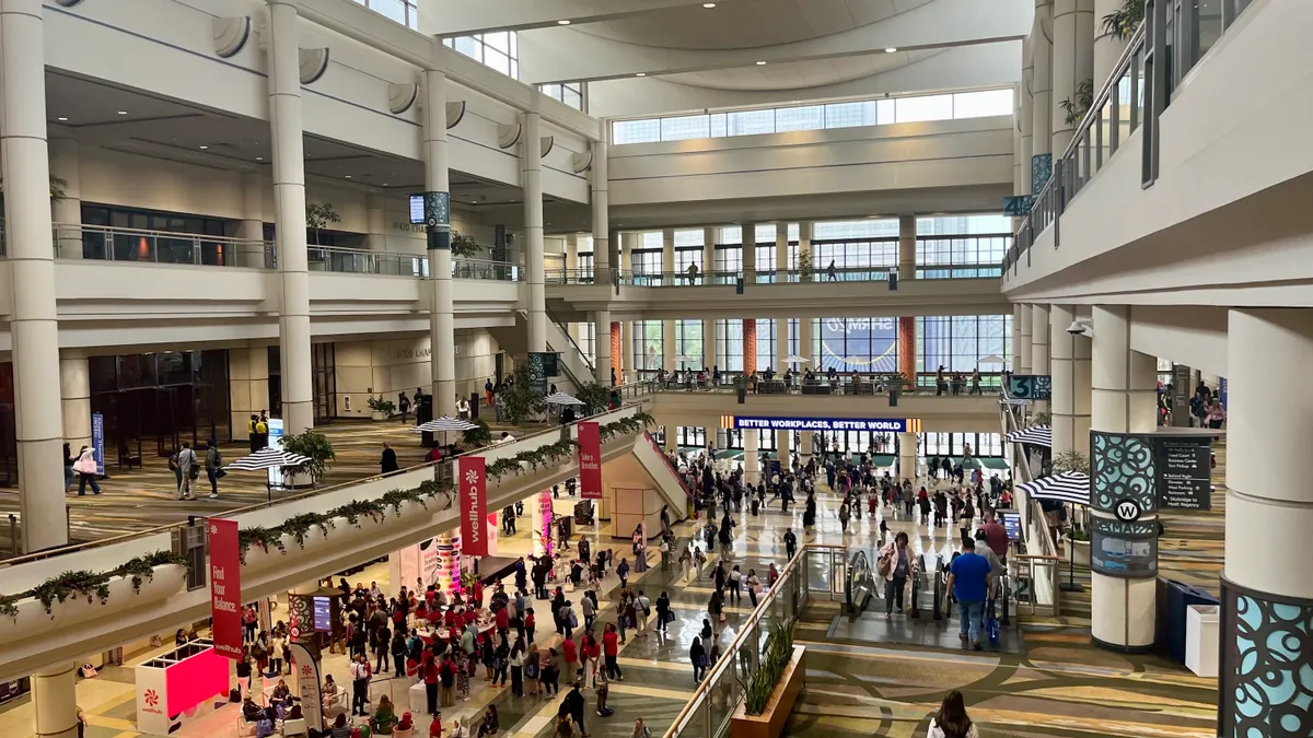 A crowd walks through a convention center, seen from a high vantage point.