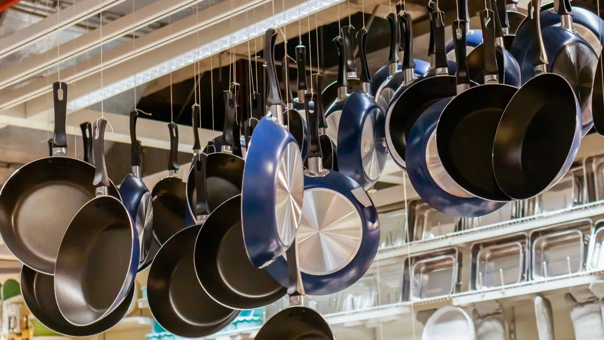 Many pans hang at various lengths from a white ceiling in a kitchen-ware store.