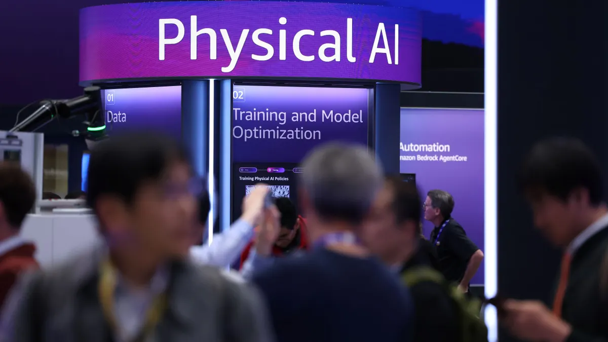 Expo attendees walk past a booth bearing signage that states "Physical AI Training and Model Optimization"