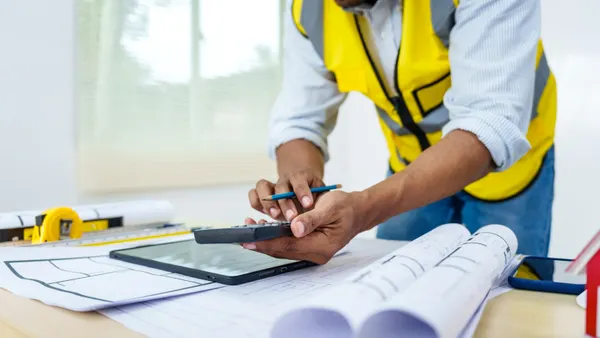 A construction worker looking over plans with a caluclator.