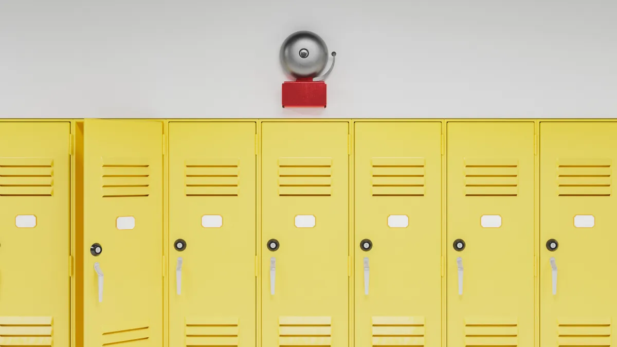 A row of yellow school lockers. Above the lockers is an old-fashioned fire alarm