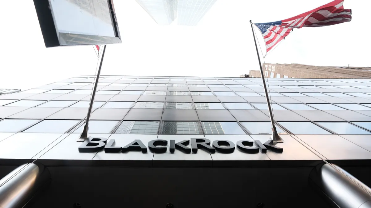 Shot of BlackRock building from below with company logo centered and U.S. flag visible to the right of company name.