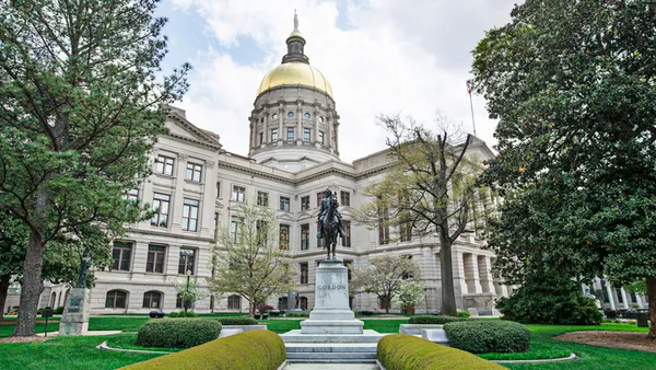 The outside of Georgia 's state capital is pictured. The facade is white and trees with green leaves surround the picture.