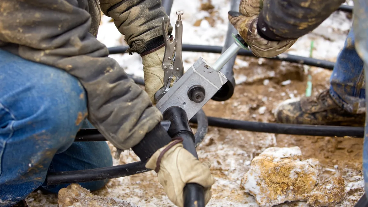 Closeup of the hands of two people holding together pipes. One pair of hands holds a tool.