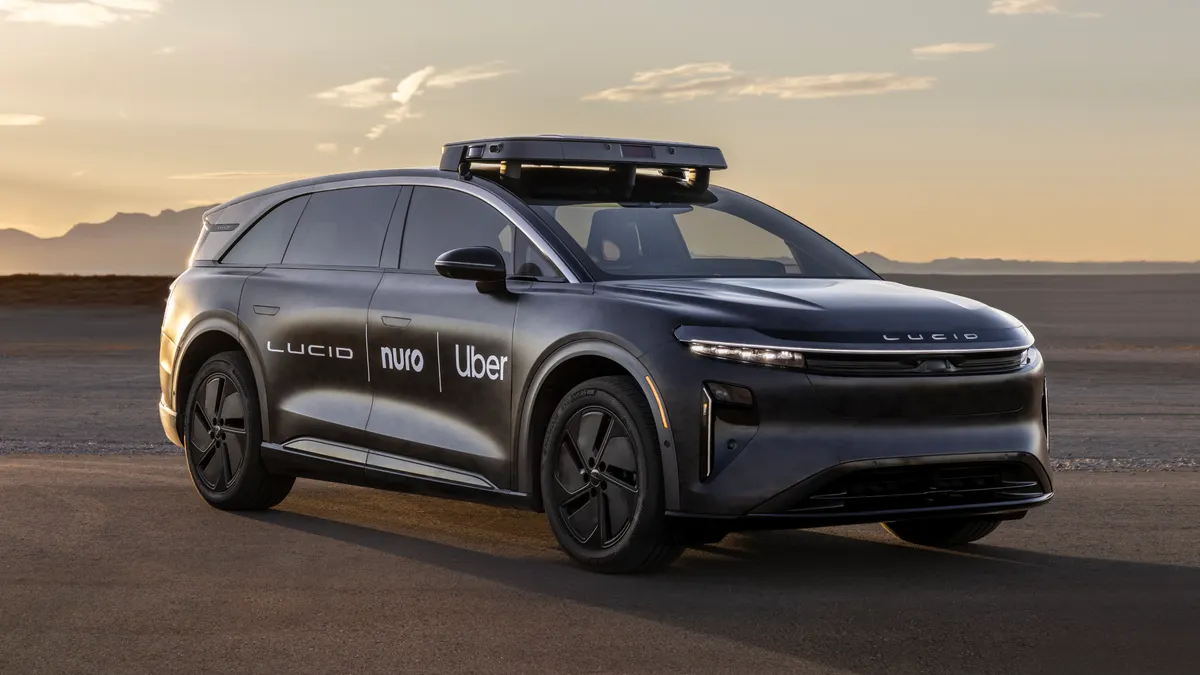 A dark gray Lucid Gravity robotaxi with the company logos of Lucid, Uber and Nuro on the right side doors.