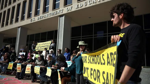 A group of people are standing outside the U.S. Department of Education with signs