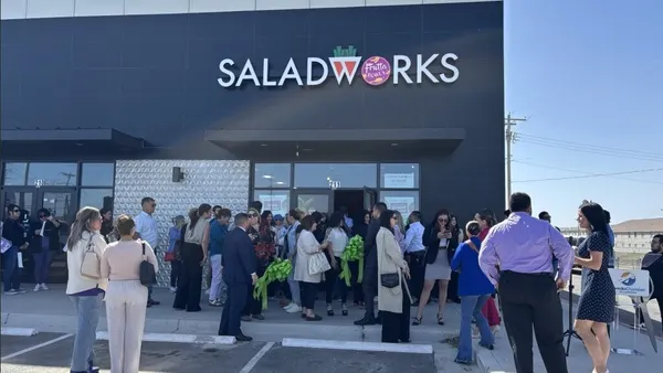 A crowd of people stand in front of a dark gray building with a logo that says Saladworks
