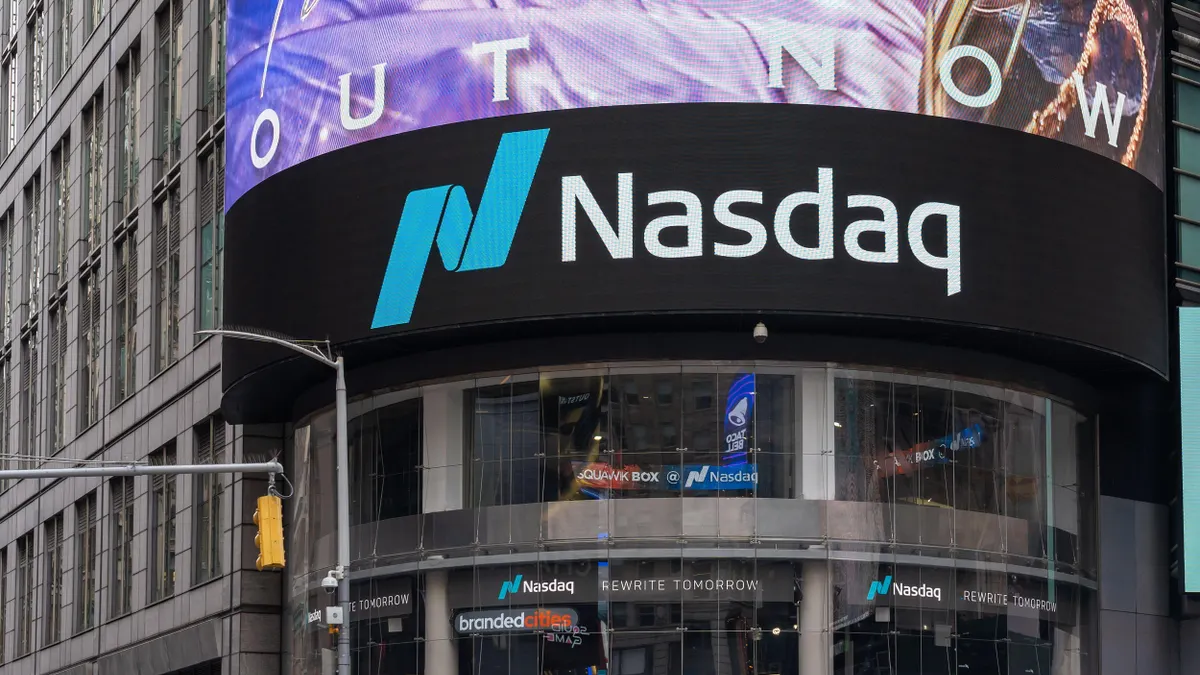 The building features a modern glass façade with the Nasdaq logo prominently displayed. Surrounding the structure are other commercial buildings and digital billboards, which are characteristic of the vibrant Times Square environment.