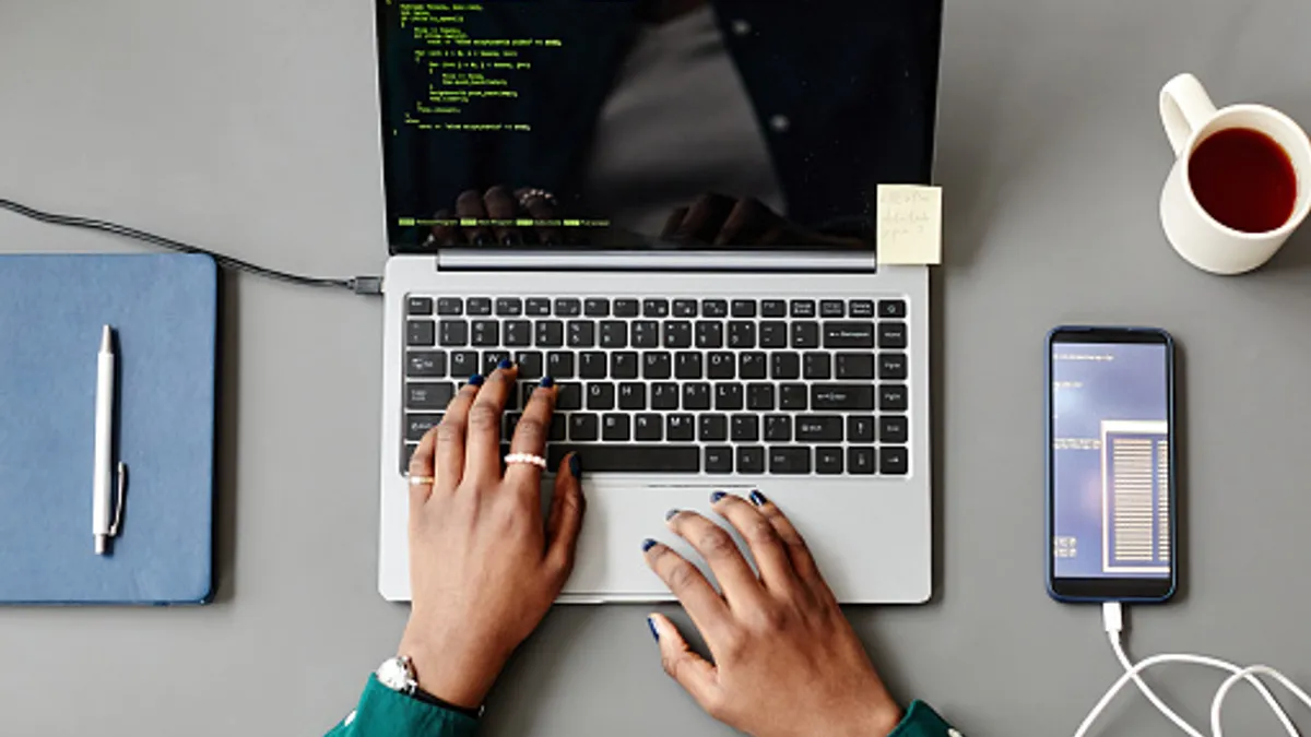 Photo taken from above looking down at someone coding on a computer with a phone charging and coffee nearby