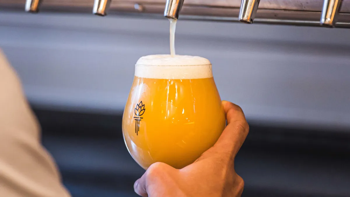 A glass goblet being held up by a hand and filled with an orange liquid on tap.