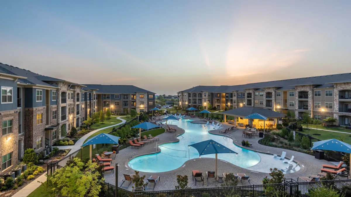 Modern three-story apartment building with balconies and a pool between buildings.