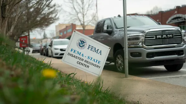 A sign that says “FEMA-STATE Disaster Recovery Center” in the grass in front of a parked pickup truck.