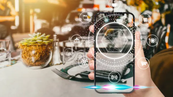 A hand holds up a smartphone with various graphics coming off of it. In the background,there is a blurred restaurant table.