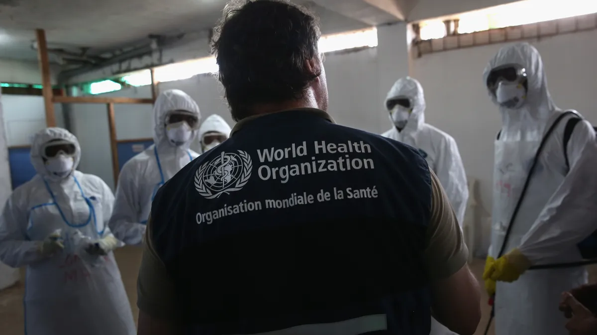 A World Health Organization  instructor teaches new health workers during a training session on October 3, 2014 in Monrovia, Liberia. His back is turned so you can see the WHO's logo on his vest.