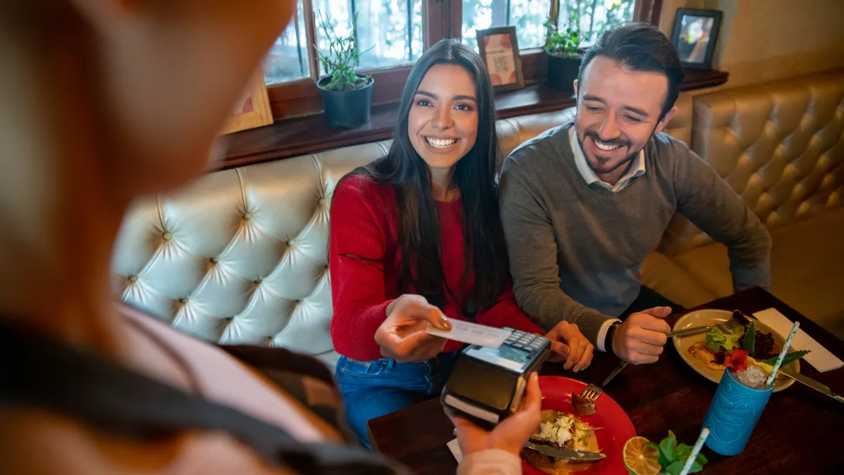 Couple eating at a restaurant and making a contactless payment to the waiter
