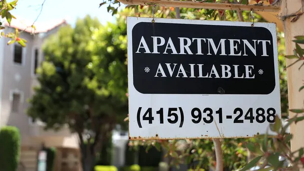 Apartment available sign hangs in front of an apartment building.