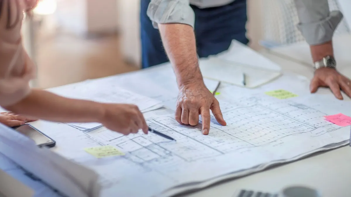 A view of construction plans, with two people pointing at the drawings.